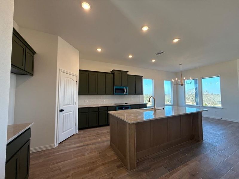 Kitchen featuring light stone countertops, hanging light fixtures, a chandelier, recessed lighting, and stainless steel microwave