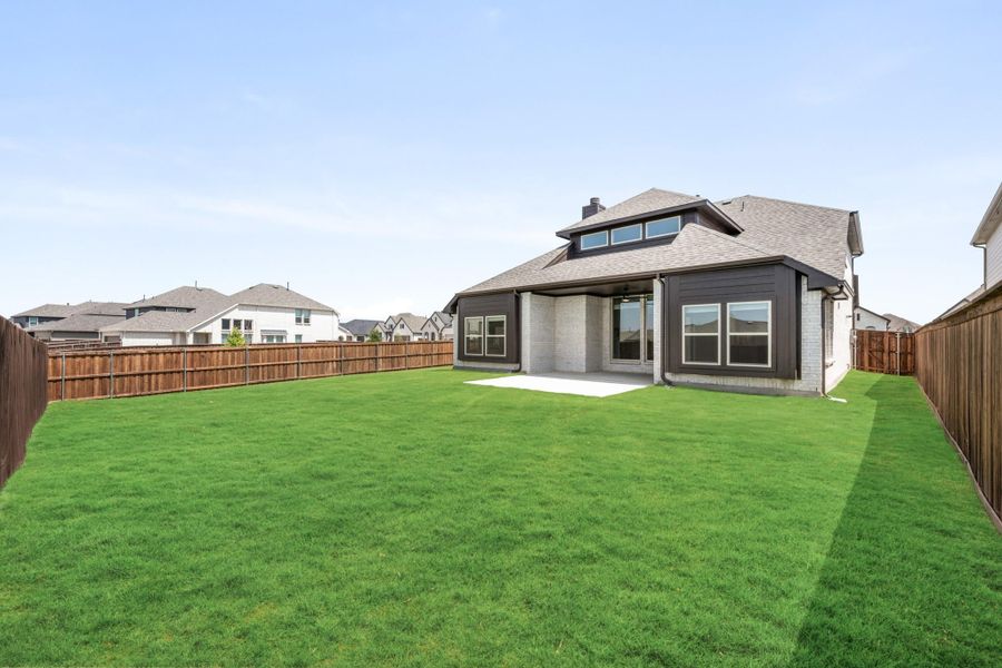 Backyard of two-story home with large green lawn, covered patio, and wood privacy fence Backyard of two-story home with large green lawn, covered patio, and wood privacy fence