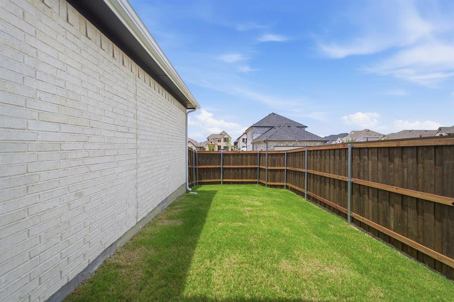 Grassed side yard featuring a light-colored brick exterior, white gutter system, and a tall wood privacy fence
