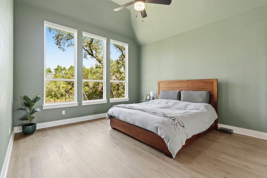 A tranquil bedroom features vaulted ceilings and light wood flooring, offering verdant views through multiple tall windows.