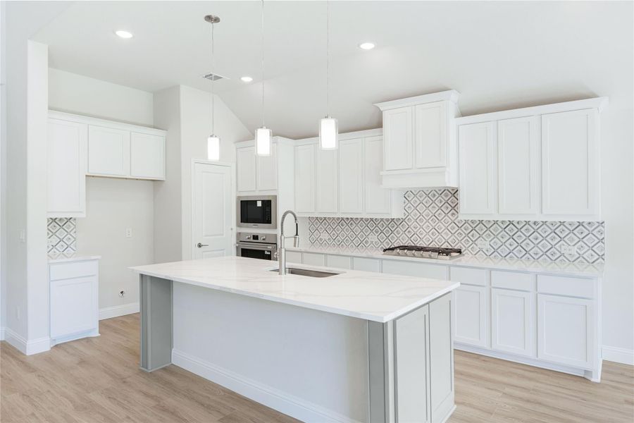 White kitchen with large island, quartz countertops, patterned tile backsplash, and stainless steel appliances