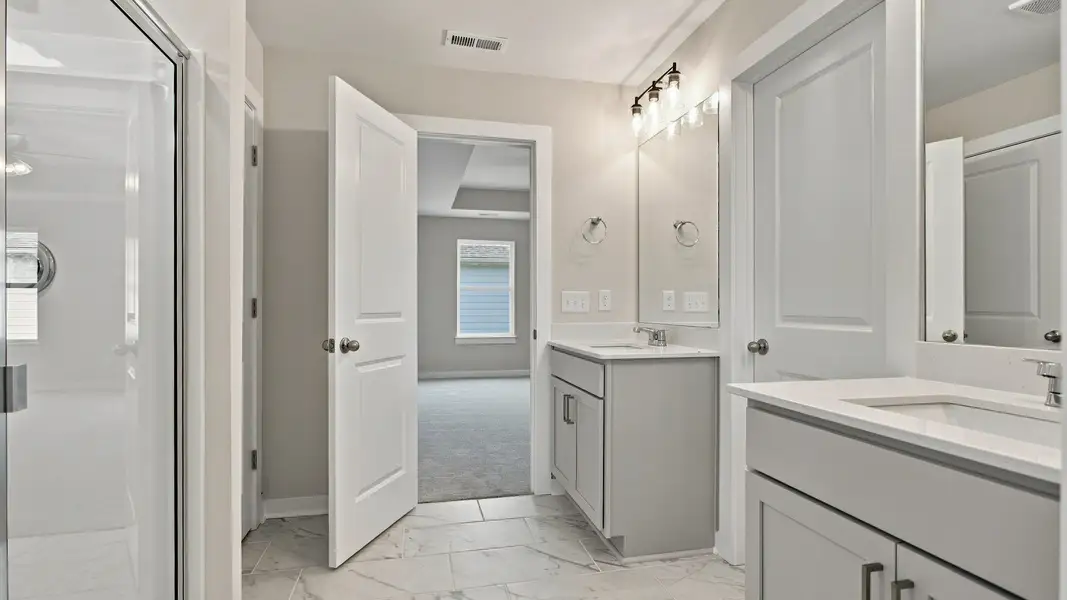 Primary bathroom entry way door next to convenient separated dual vanities