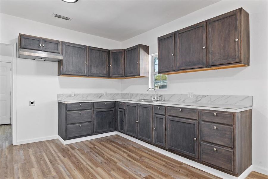 Kitchen featuring light countertops, dark brown cabinets, light wood finished floors, and under cabinet range hood Kitchen featuring light countertops, dark brown cabinets, light wood finished floors, and under cabinet range hood