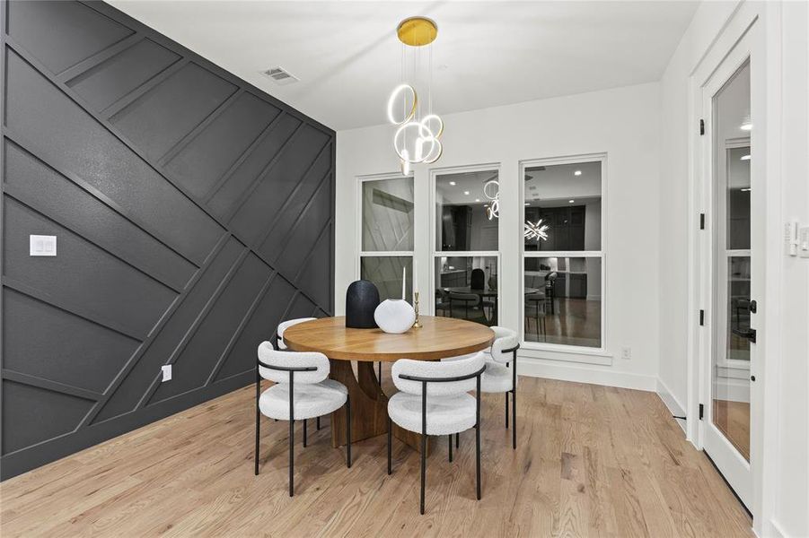 Dining area with light wood-style floors, visible vents, a decorative wall, and a notable chandelier