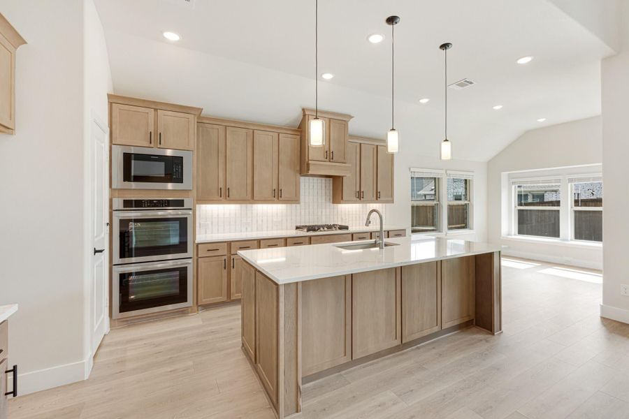 Kitchen with light wood cabinets, large island, stainless steel appliances, and pendant lights over white countertops