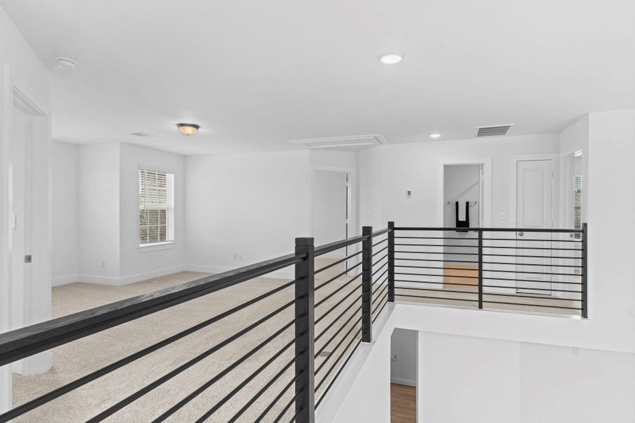 The spacious upstairs game room is a versatile retreat perfect for entertaining, relaxing, or setting up a media space. With soft carpeting, sleek wrought iron catwalk, and natural light pouring in from multiple windows, this open and airy space serves as a central hub on the second floor. **Image Representative of Plan Only and May Vary as Built**.