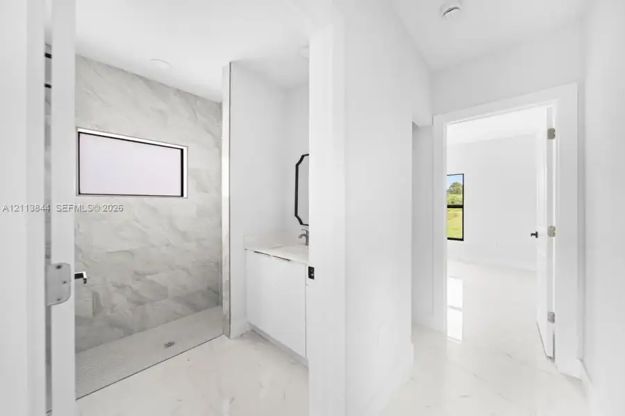 Walk-in shower featuring large-format tile walls, recessed lighting, and a pebble-tiled floor, complemented by a white vanity with a stone countertop and light-colored tile flooring Walk-in shower featuring large-format tile walls, recessed lighting, and a pebble-tiled floor, complemented by a white vanity with a stone countertop and light-colored tile flooring