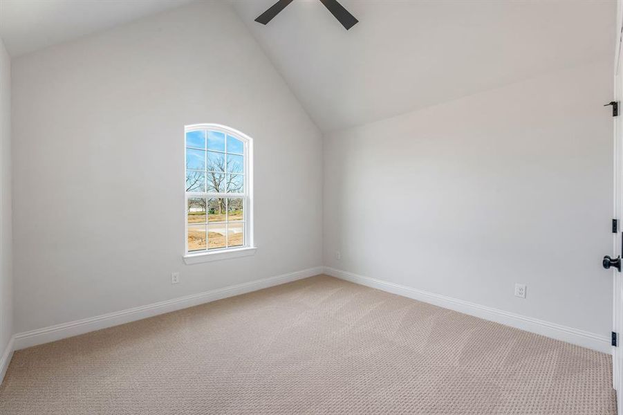 Empty room with ceiling fan, carpet floors, and high vaulted ceiling