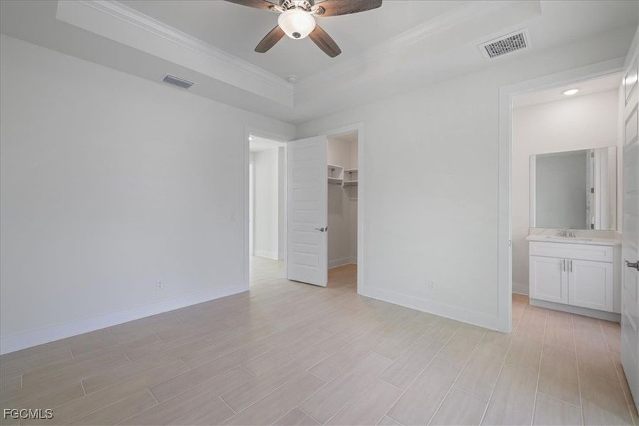 Unfurnished bedroom with a raised ceiling, a spacious closet, connected bathroom, wood finish floors, and ceiling fan