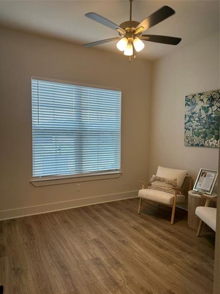 Neutral wall paint with wood-finish flooring, featuring a window with horizontal blinds, a ceiling fan with integrated lighting, and white baseboards