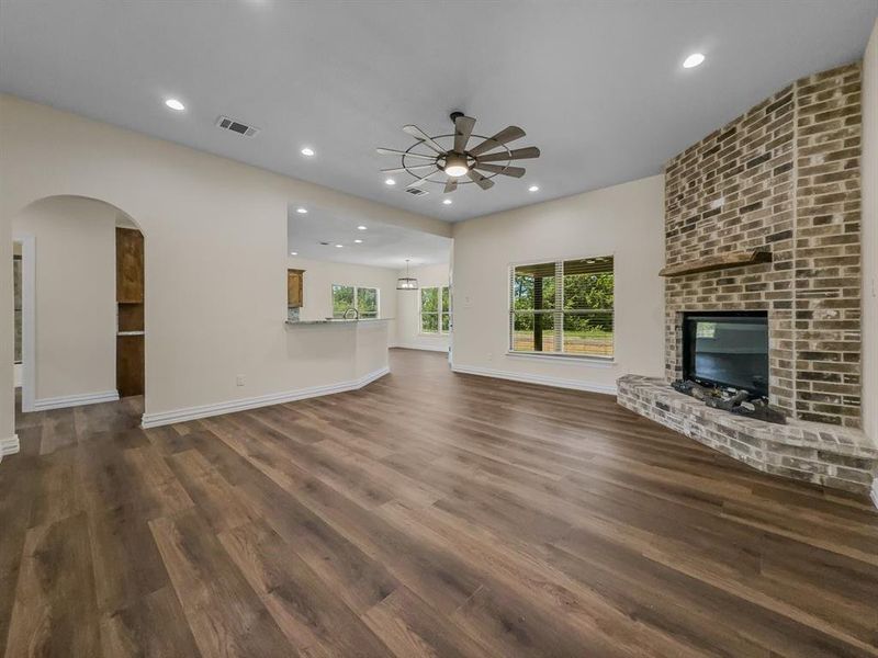 Unfurnished living room with ceiling fan, dark wood finished floors, recessed lighting, a fireplace, and arched walkways Unfurnished living room with ceiling fan, dark wood finished floors, recessed lighting, a fireplace, and arched walkways