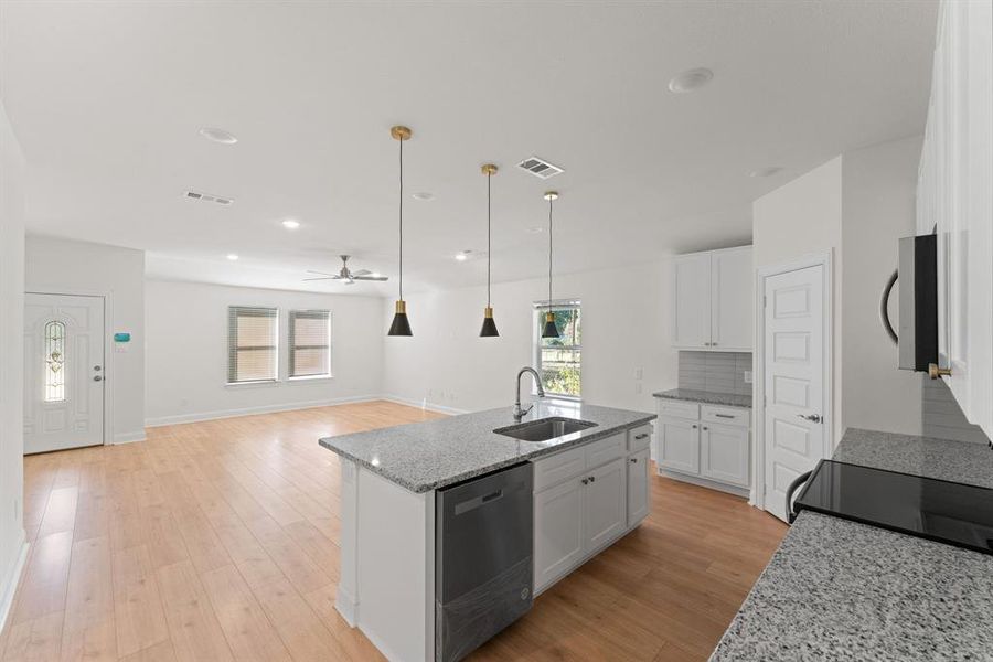 Kitchen with hanging light fixtures, a center island with sink, white cabinetry, dishwasher, and sink