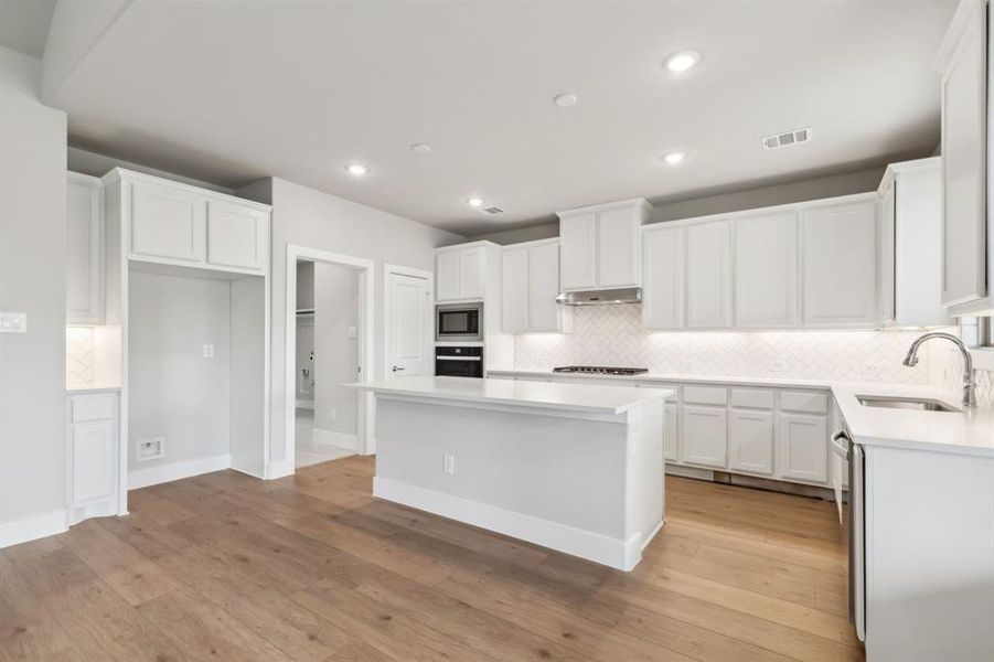 Kitchen with appliances with stainless steel finishes, light wood-type flooring, sink, a center island, and white cabinetry