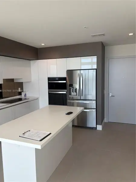 Kitchen featuring a central island with a solid surface countertop, high-gloss white cabinetry, stainless steel appliances including a built-in wall oven, and ceramic tile flooring