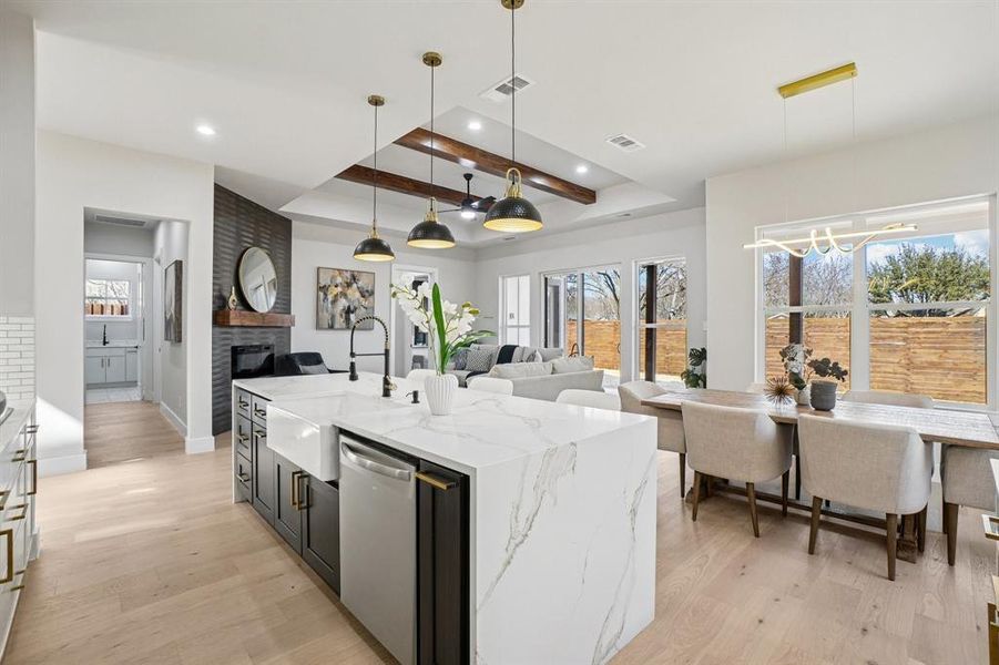 Dual tone kitchen featuring light stone counters, decorative light fixtures, open floor plan, a center island with sink, and dishwasher