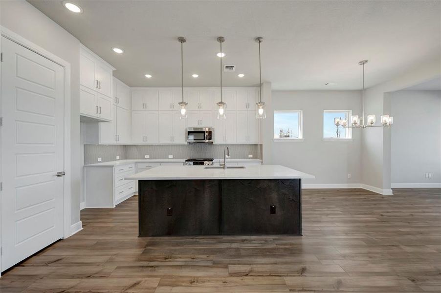 Two tone kitchen with an island with sink, dark wood-type flooring, stainless steel appliances, two tone cabinets, and backsplash