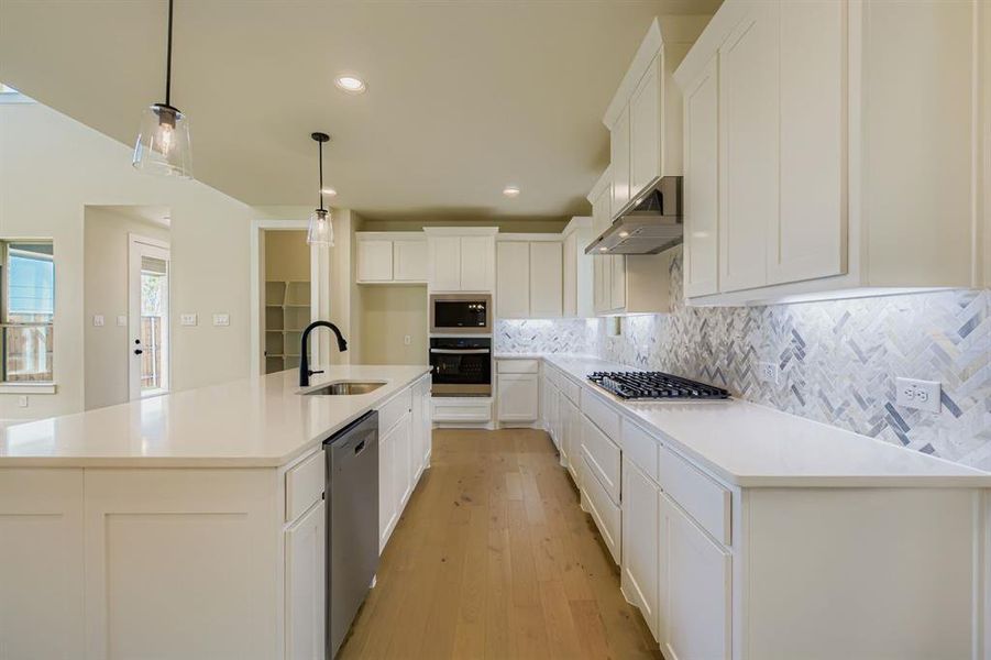Kitchen featuring tasteful backsplash, a kitchen island with sink, white cabinets, hanging light fixtures, and stainless steel appliances