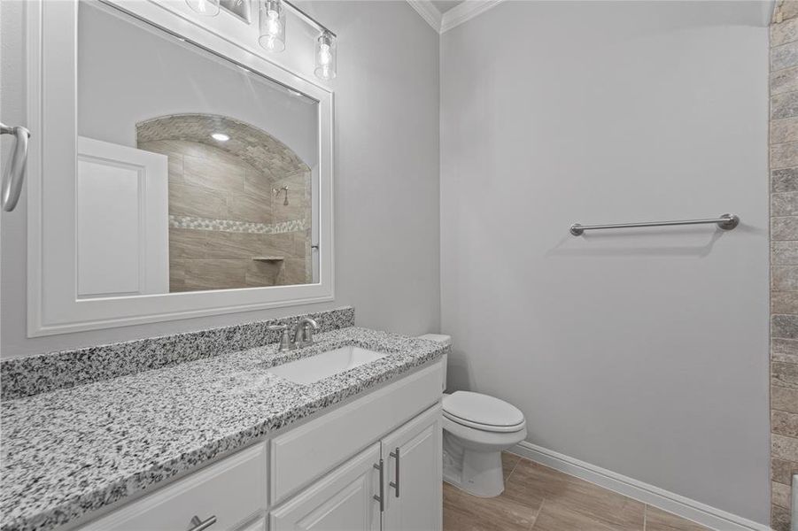 Bathroom featuring vanity, toilet, crown molding, and tiled shower