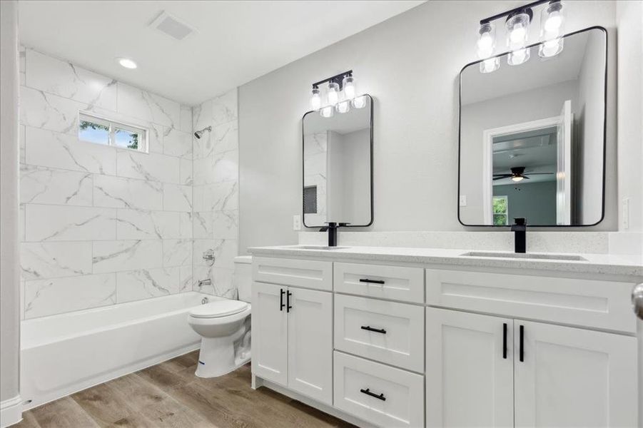 Full bathroom featuring tiled shower / bath, double vanity, toilet, ceiling fan, and hardwood / wood-style flooring