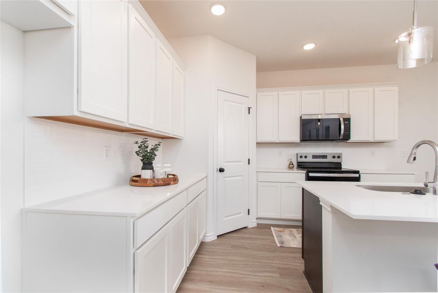 Kitchen with decorative light fixtures, white cabinetry, stainless steel appliances, light wood-style floors, and light stone counters