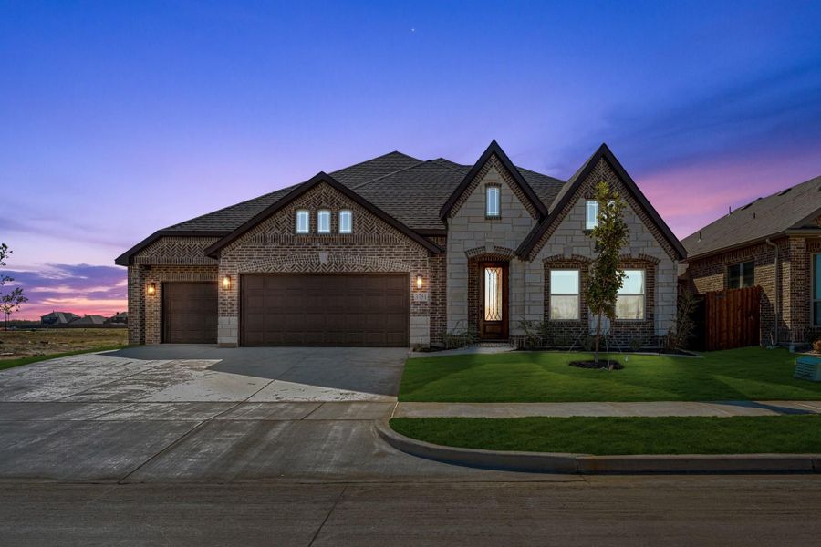 Single-story brick and stone home with three-car garage, arched windows, and front lawn at dusk Single-story brick and stone home with three-car garage, arched windows, and front lawn at dusk