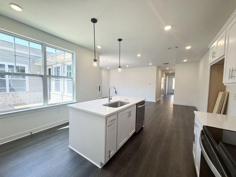 Kitchen with white cabinets, dark wood-type flooring, an island with sink, decorative light fixtures, and stainless steel appliances