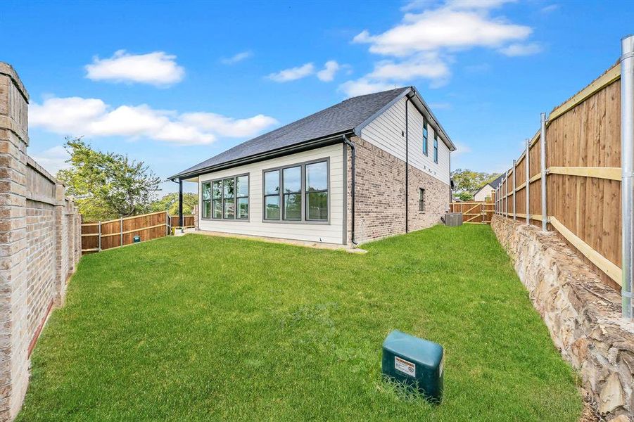 Rear view of house with a fenced backyard, brick siding, and roof with shingles