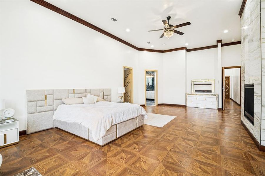 Spacious primary bedroom featuring patterned wood-finish flooring, recessed lighting, and a prominent fireplace with a stone-clad surround