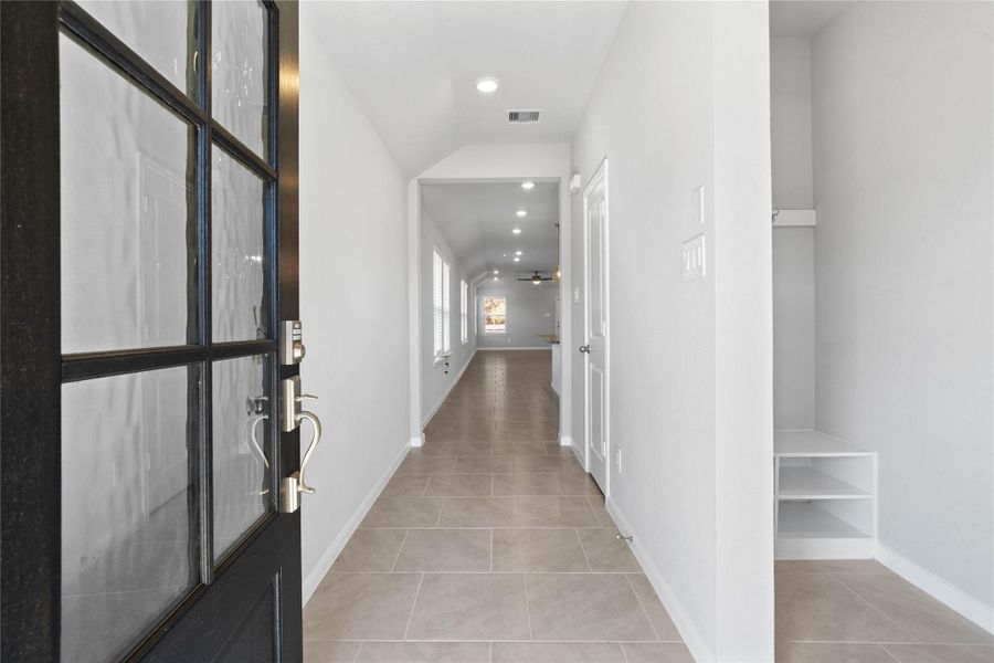 This entryway features a modern, open-concept design. The long, bright corridor utilizes a neutral color palette, recessed lighting, and floor tiles to lead the eye toward the home's main living area.