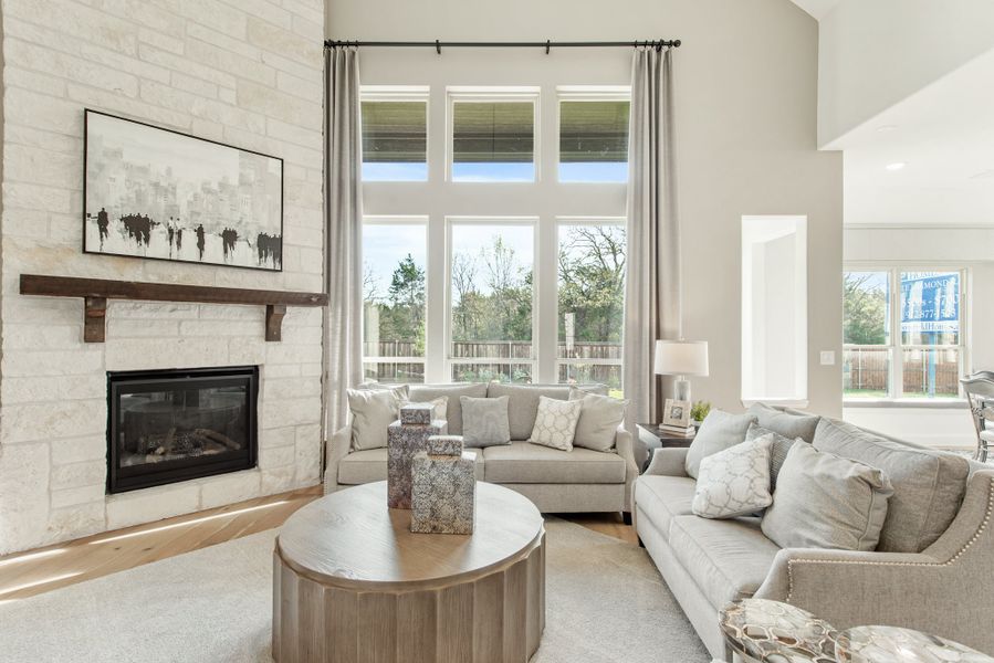 Living room with stone fireplace, high ceilings, large windows, and gray sofas around a round wood coffee table Living room with stone fireplace, high ceilings, large windows, and gray sofas around a round wood coffee table