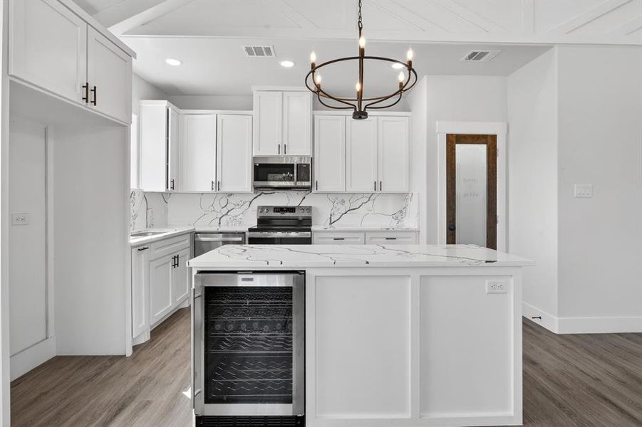 Modern kitchen featuring a central island with an integrated beverage cooler, sleek white cabinetry with dark hardware, stone countertops with a striking veined pattern, stainless steel appliances, and wood-finish flooring