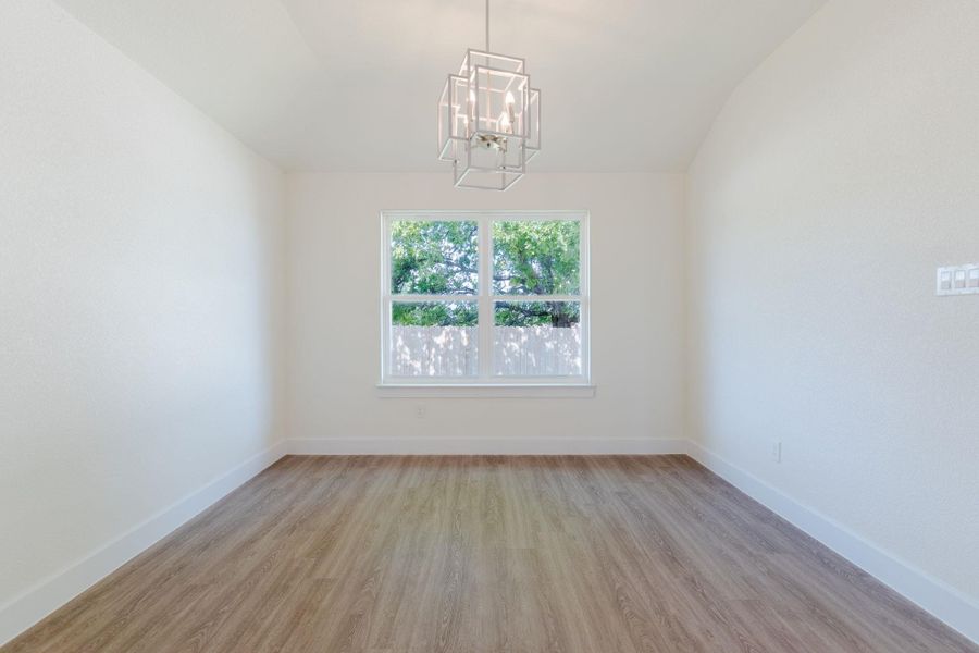 Empty room featuring light wood-type flooring, a chandelier, and vaulted ceiling
