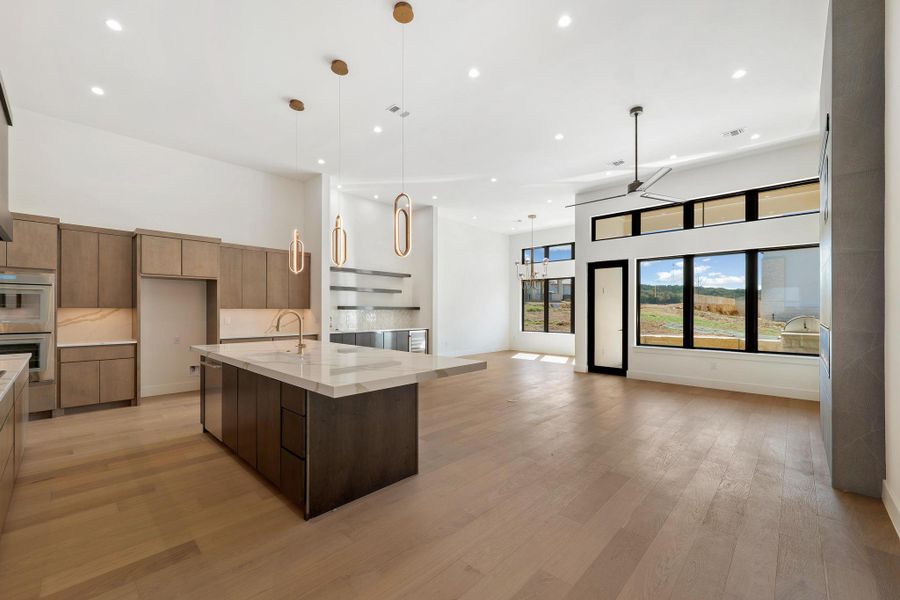 Kitchen featuring a high ceiling, modern cabinets, open floor plan, hanging light fixtures, and light wood finished floors
