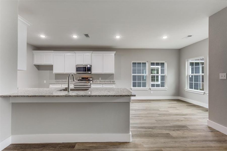 Kitchen with white cabinetry, light stone countertops, appliances with stainless steel finishes, recessed lighting, and light wood-style floors