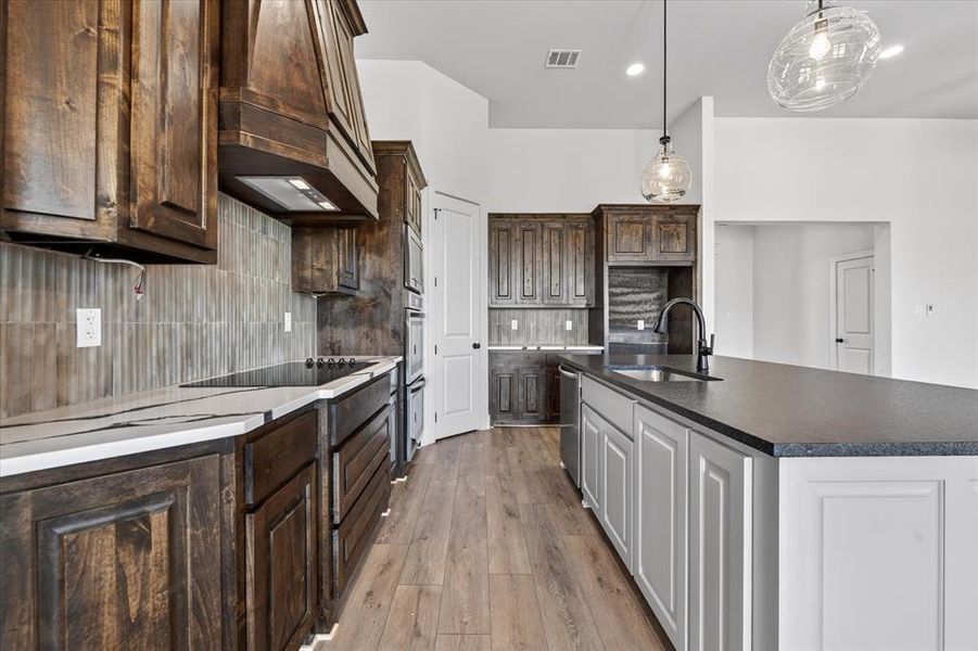 Kitchen featuring light wood-style floors, an island with sink, pendant lighting, two tone cabinetry, and decorative backsplash