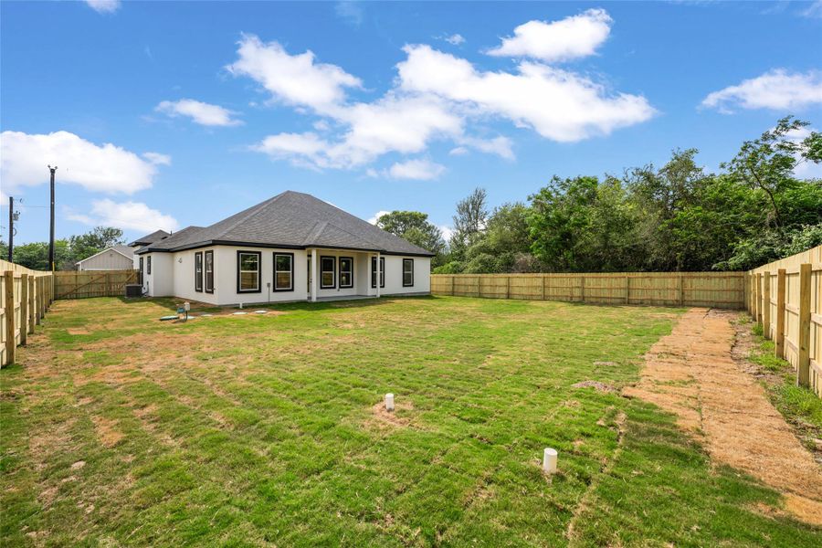 Spacious backyard featuring a newly installed wooden privacy fence, a newly constructed residence with a dark shingle roof, and multiple rear-facing windows