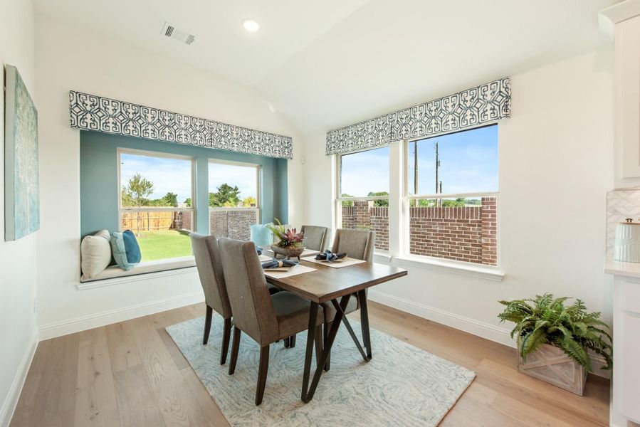 Dining area with wood table, four chairs, window seat, and large windows with backyard view on light hardwood floors Dining area with wood table, four chairs, window seat, and large windows with backyard view on light hardwood floors