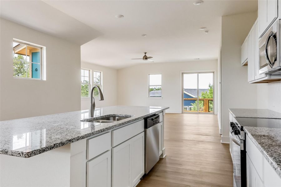 Kitchen with white cabinetry, light stone counters, stainless steel appliances, and light wood-style floors