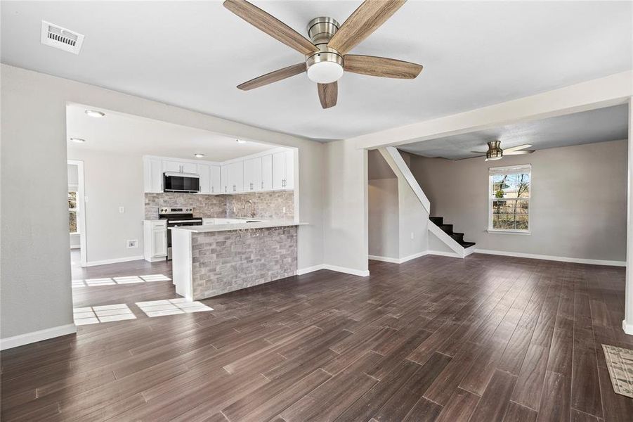 Unfurnished living room featuring ceiling fan, dark wood-style flooring, and stairs