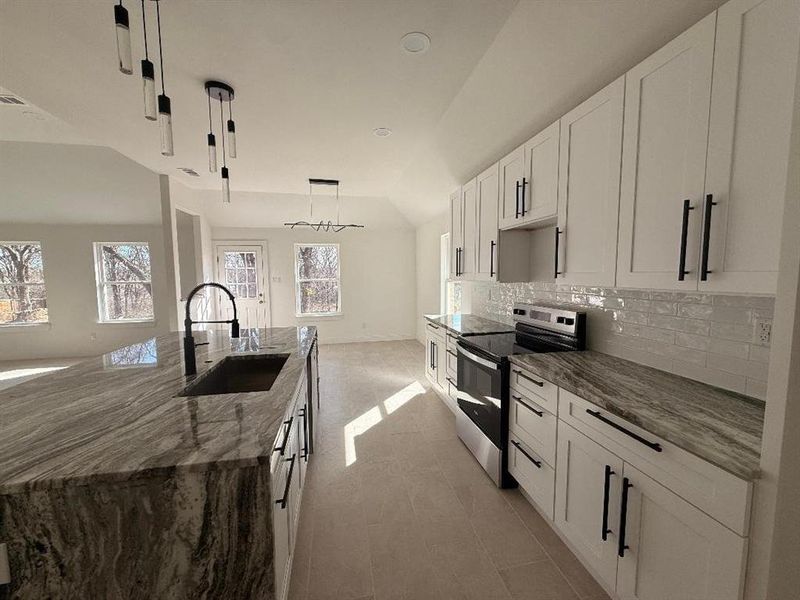 Kitchen with stainless steel range with electric stovetop, a center island with sink, dark stone counters, lofted ceiling, and white cabinetry