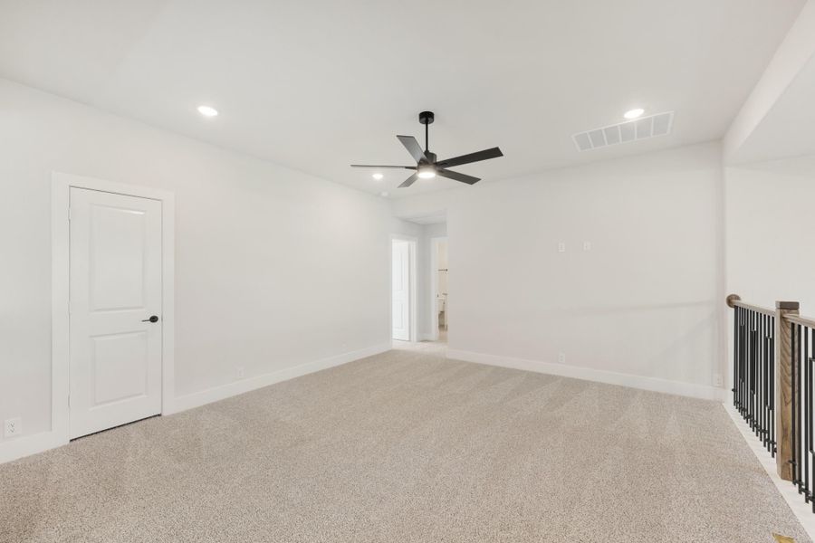 Empty room with beige carpet, ceiling fan, white walls, and staircase railing visible on the right