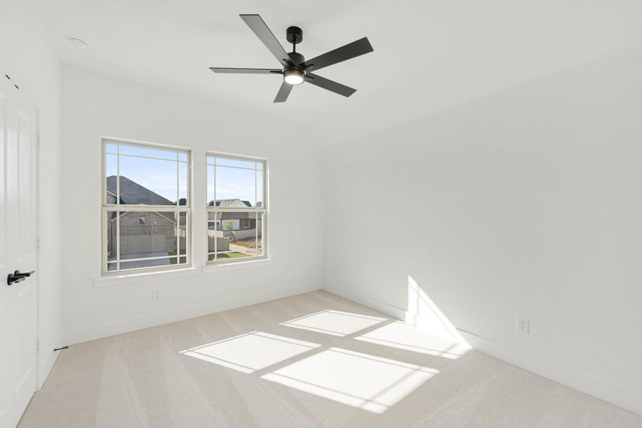 Empty bedroom with white walls, carpet flooring, ceiling fan, and two windows with natural light