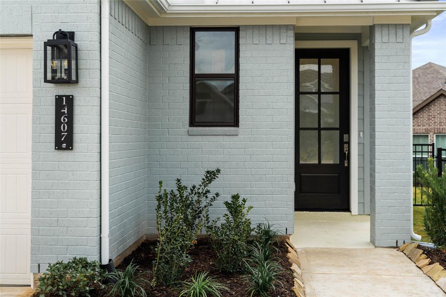 As you walk up to this beautiful home, you notice the painted brick elevation with modern farmhouse style. The main entry features a sophisticated black door with clear glass, allowing natural light into the foyer. The dark window and door frame, exterior light and address number plate create a crisp, contemporary contrast and curb appeal.