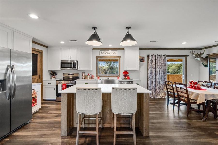 Open-concept kitchen featuring white cabinetry, stainless steel appliances, and wood-finish flooring