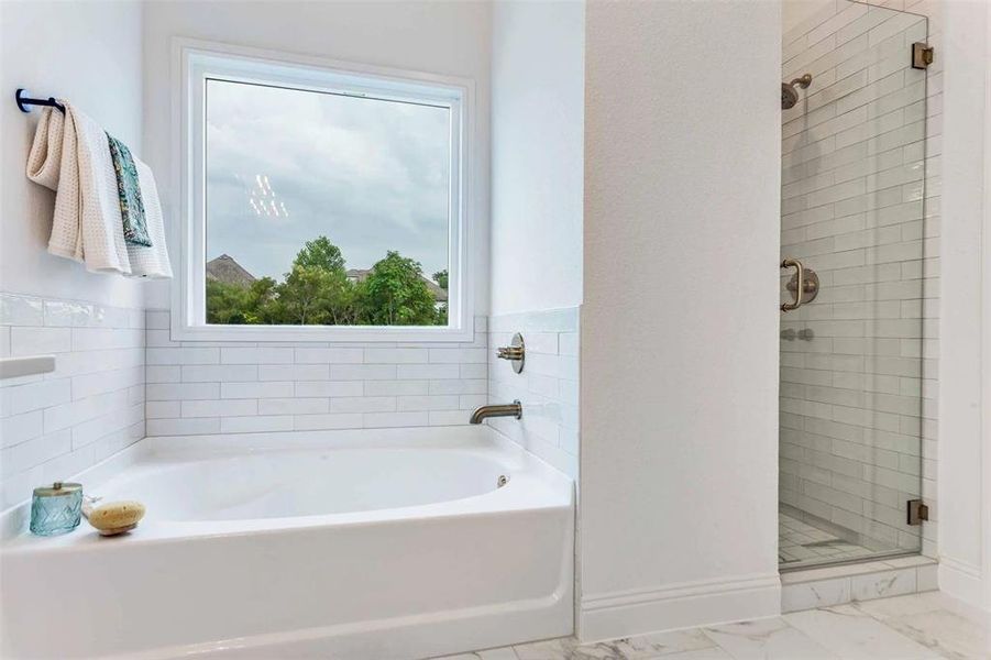 Full bath featuring a stall shower, a garden tub, and light marble finish flooring