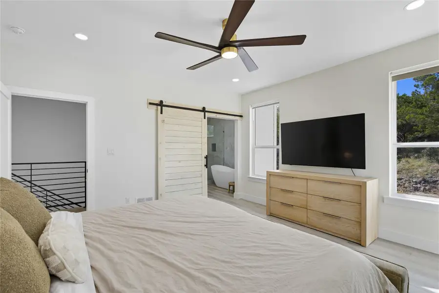 Bedroom with a barn door, recessed lighting, ceiling fan, ensuite bathroom, and light wood finished floors