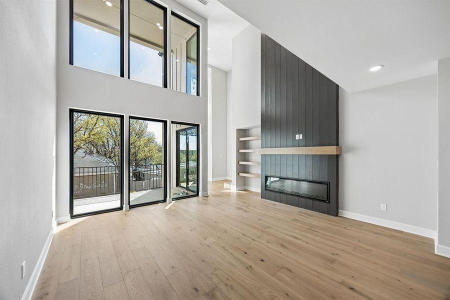 Unfurnished living room with a fireplace, a high ceiling, light wood-type flooring, and recessed lighting Unfurnished living room with a fireplace, a high ceiling, light wood-type flooring, and recessed lighting