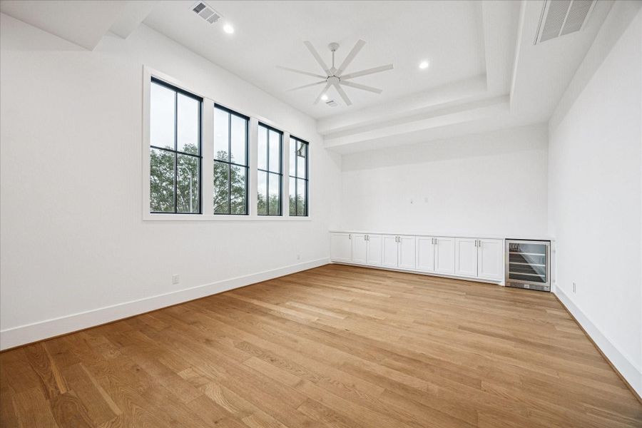 Spacious upstairs game room designed for versatile living and entertainment. Sunlight pours through an extended row of picture windows, highlighting the wide-plank hardwood floors and subtle tray ceiling detail. Custom built-ins with abundant closed storage and a beverage fridge create a functional hub for movie nights, play space, or casual gatherings. Its open layout flows seamlessly into the upstairs landing, giving the entire second floor a bright, connected feel. Spacious upstairs game room designed for versatile living and entertainment. Sunlight pours through an extended row of picture windows, highlighting the wide-plank hardwood floors and subtle tray ceiling detail. Custom built-ins with abundant closed storage and a beverage fridge create a functional hub for movie nights, play space, or casual gatherings. Its open layout flows seamlessly into the upstairs landing, giving the entire second floor a bright, connected feel.
