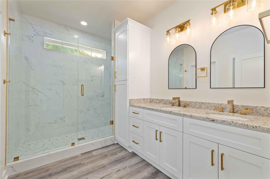 Full bath featuring double vanity, a marble finish shower, light wood-type flooring, and recessed lighting Full bath featuring double vanity, a marble finish shower, light wood-type flooring, and recessed lighting