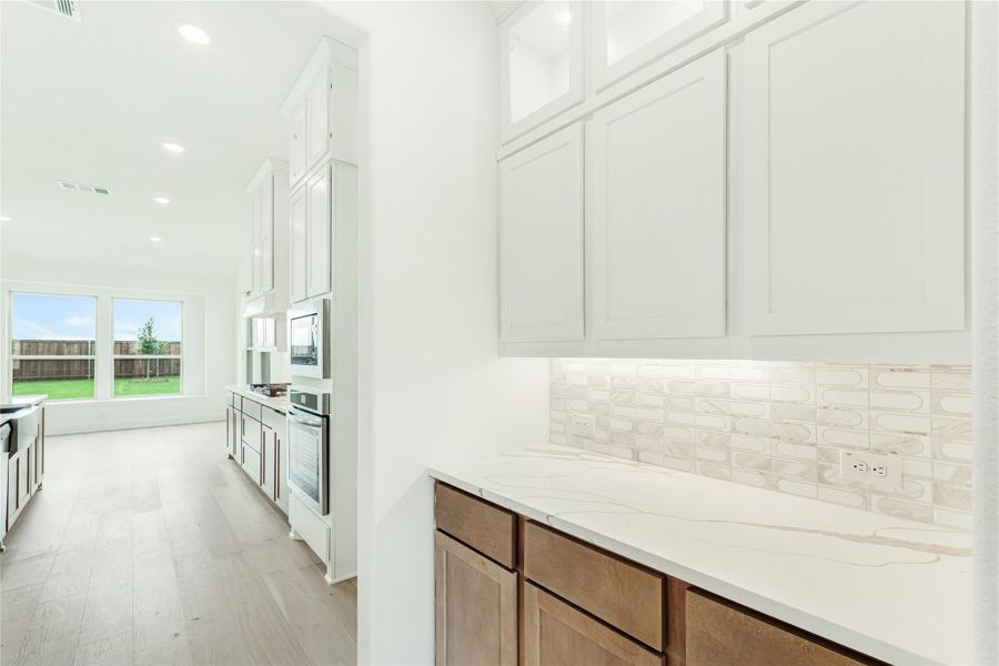 Kitchen with white upper cabinets, quartz countertops, tile backsplash, and light wood lower cabinets with stainless appliances visible.